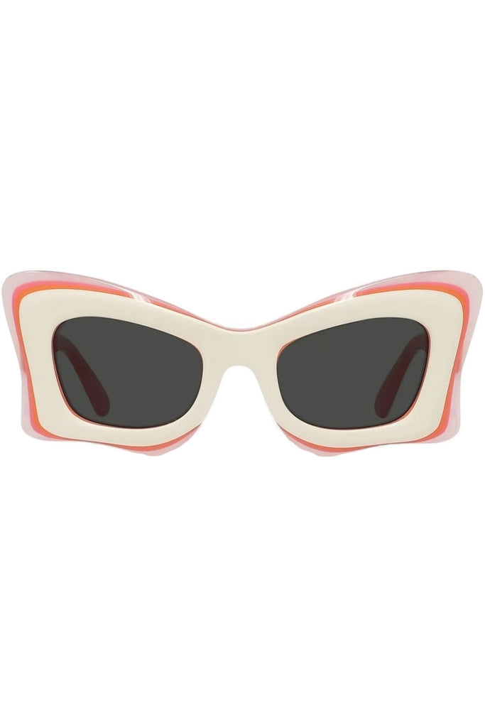 A pair of chunky, layered cat-eye sunglasses with a cream-colored frame, a coral-pink middle layer, and a thin orange outer layer, paired with dark lenses.