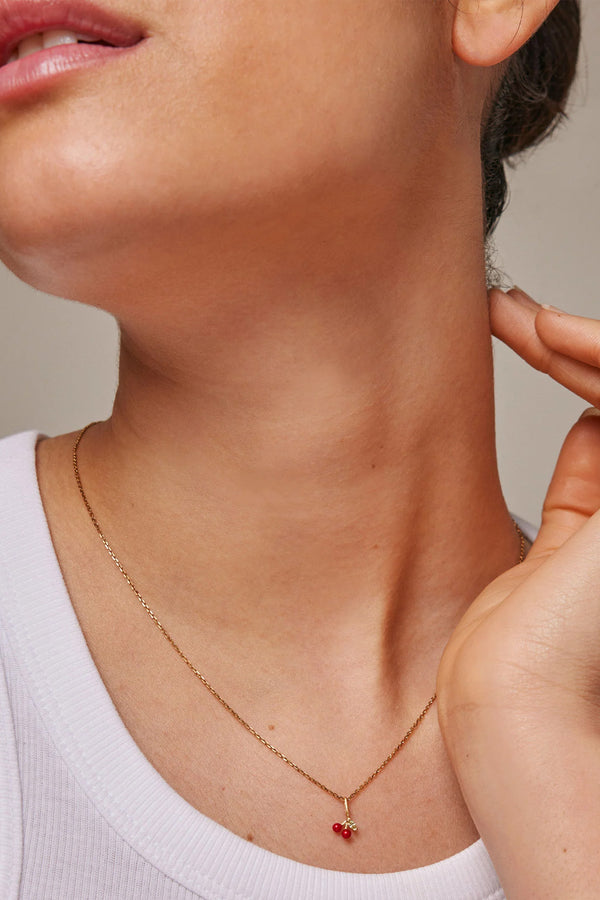 Model wearing the cherry necklace in gold and red colour from the brand ENAMEL COPENHAGEN